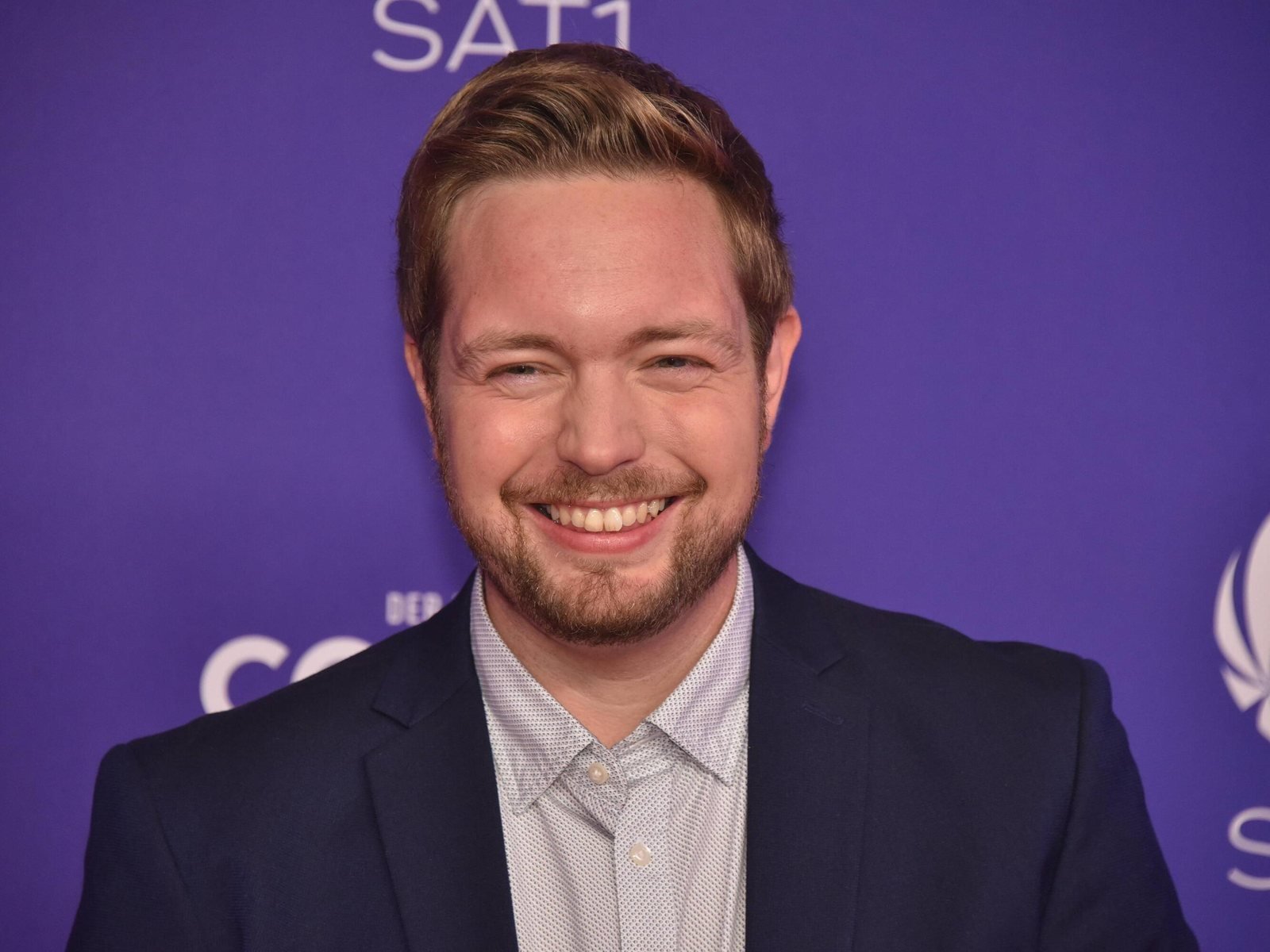 Bastian Bielendorfer lächelt bei einem Pressetermin vor einer SAT.1-Wand