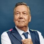Roland Kaiser im Porträt vor blauem Hintergrund, mit Weste und Krawatte