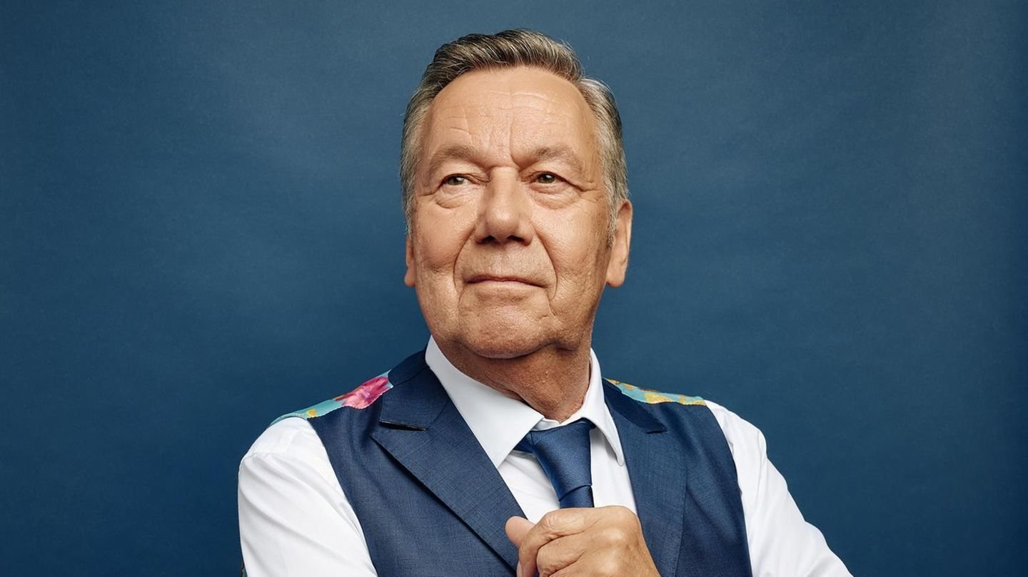 Roland Kaiser im Porträt vor blauem Hintergrund, mit Weste und Krawatte
